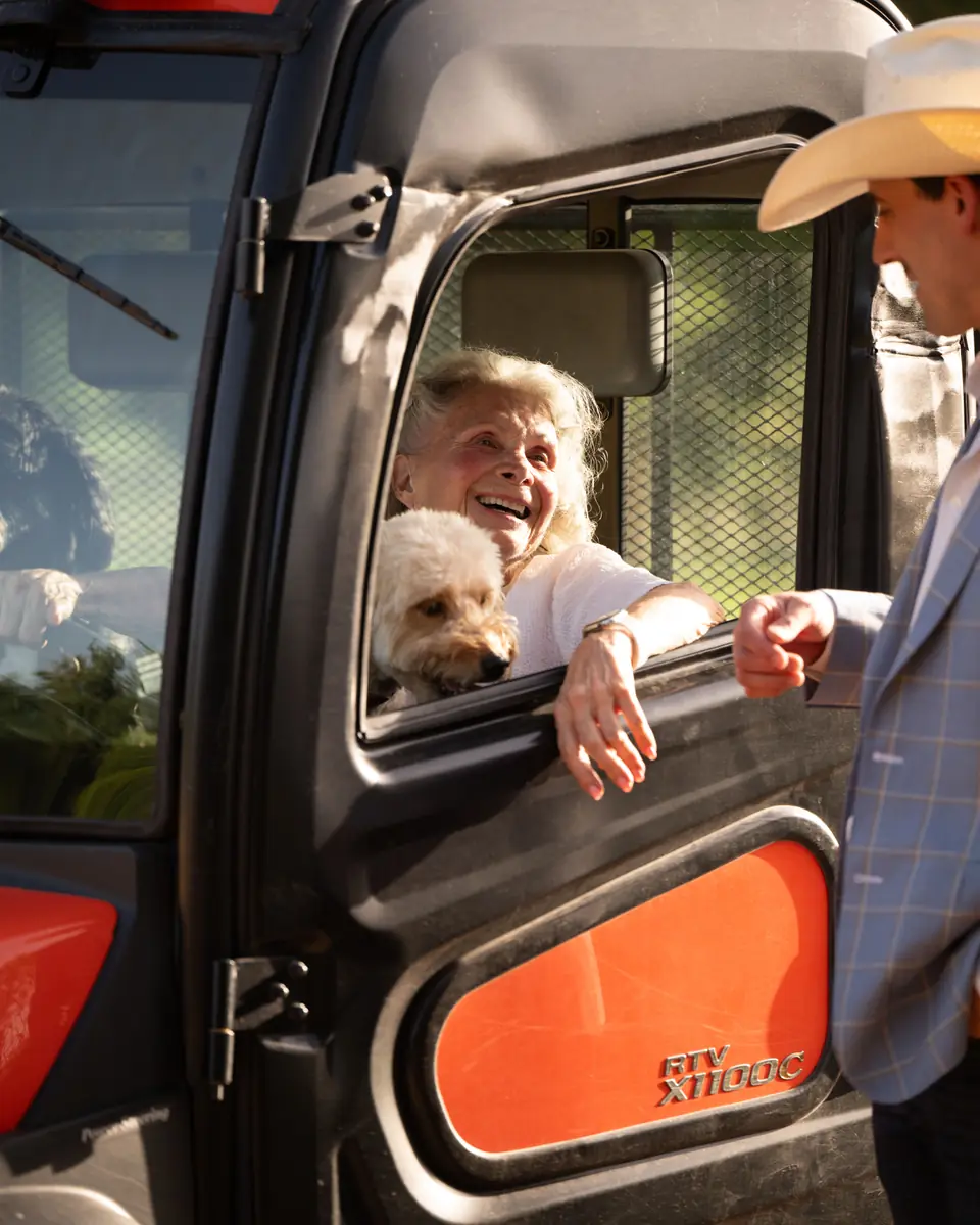 Smiling woman and her dog in a side-by-side, talking with a man in a cowboy hat on a Texas property
